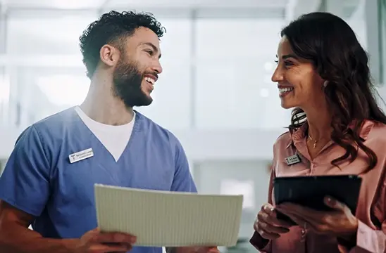 Healthcare professional and business colleague discussing patient care with digital tablet in modern hospital corridor Mobile