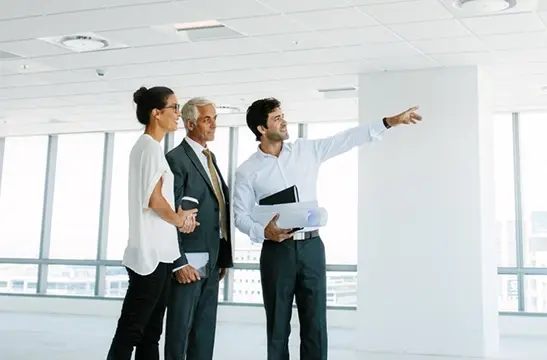 Business professionals and architect reviewing blueprints and pointing at construction plans in bright modern office space Mobile